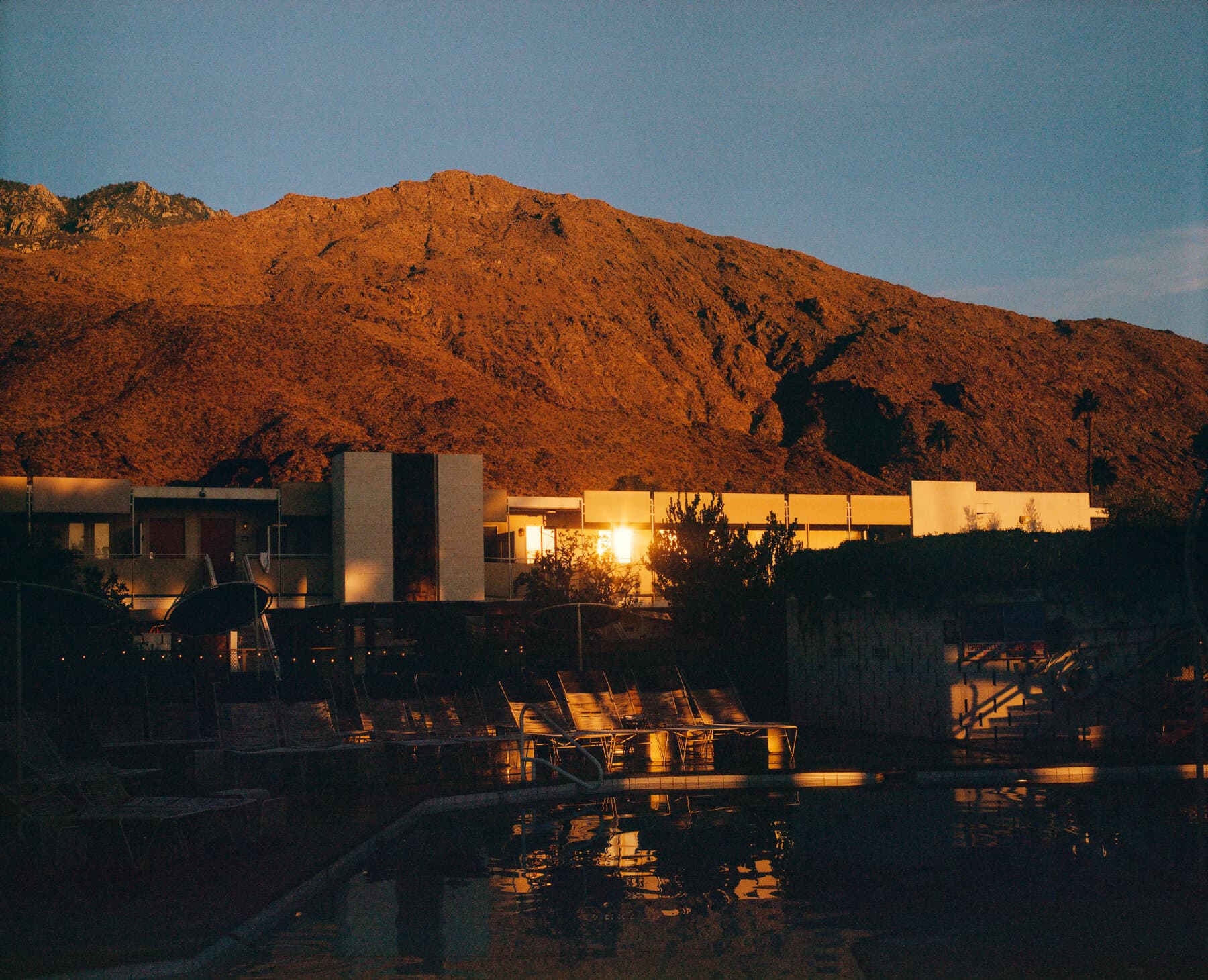 Ace Hotel & Swim Club at dusk: the San Jacinto mountains glowing warm above the lit room blocks and pool