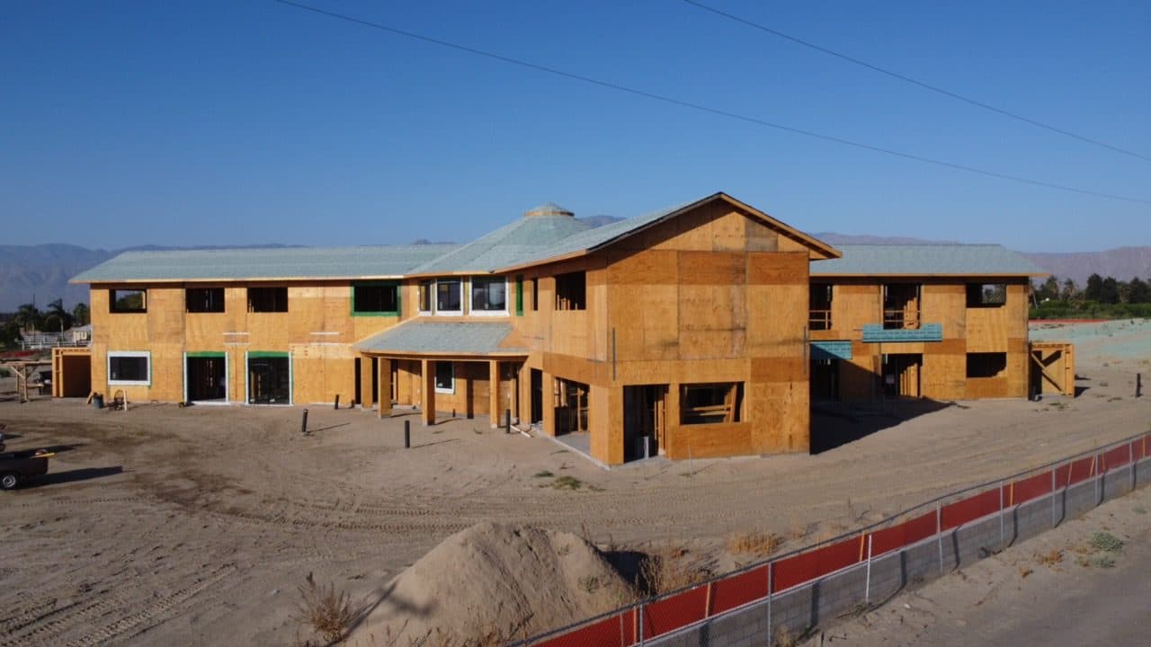 Front elevation nearly dried in: sheathed two-story walls and roofing on the central round mass and both wings.