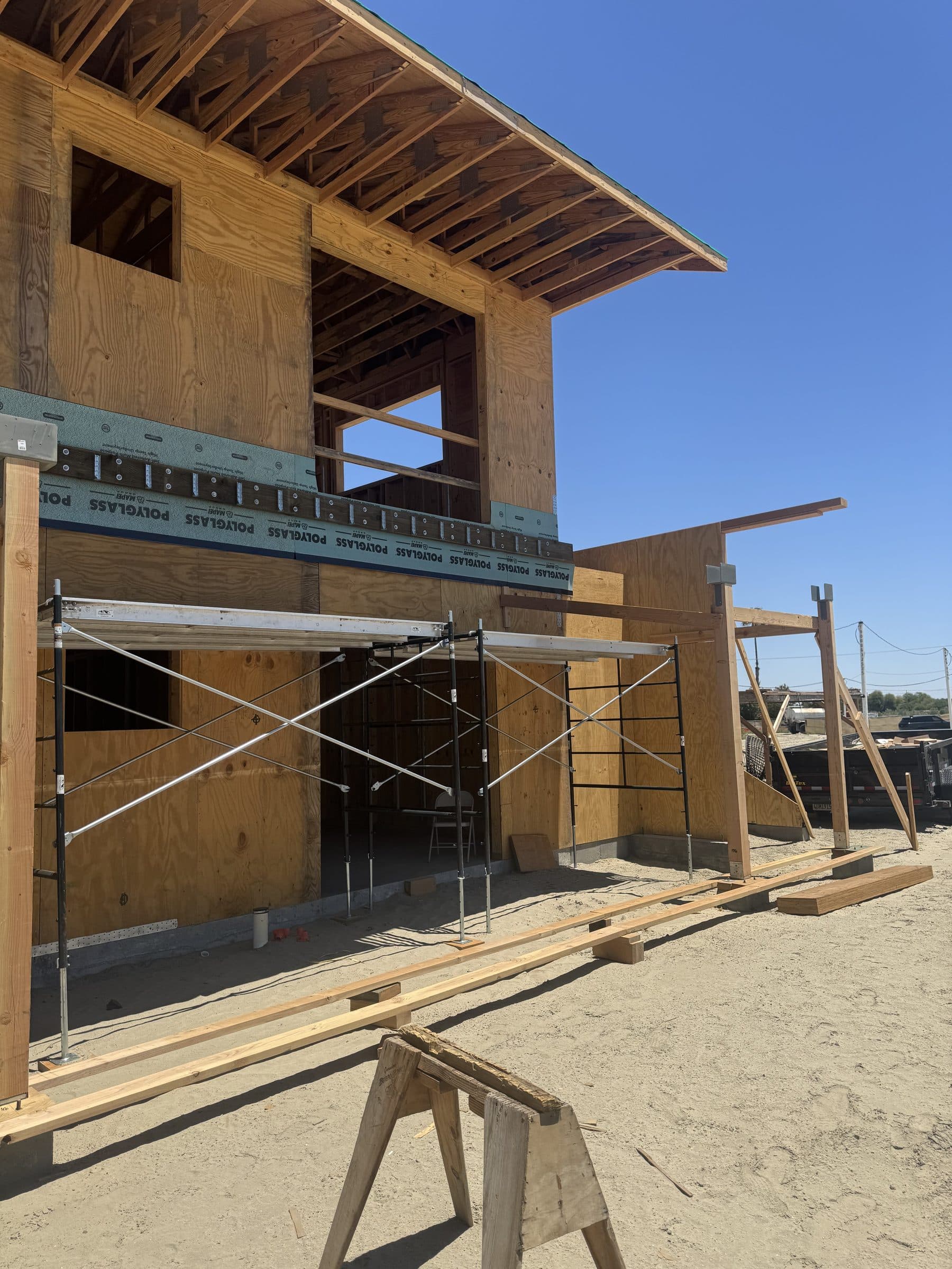 Two-story exterior wall in framing behind scaffolding, green seam strips across the fresh sheathing.