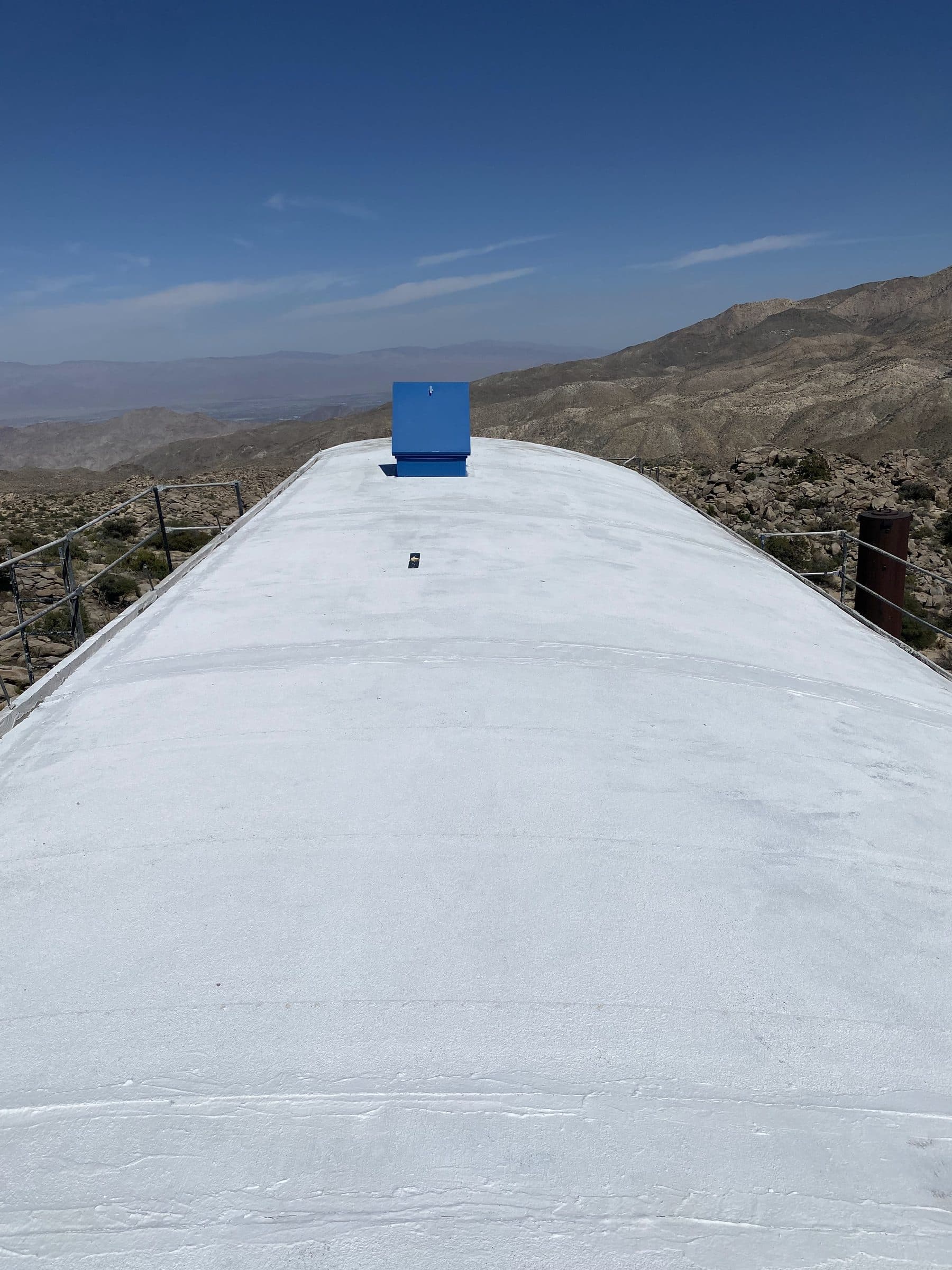 White-coated curved roof ridge with a single blue hatch, desert ranges layered beyond.