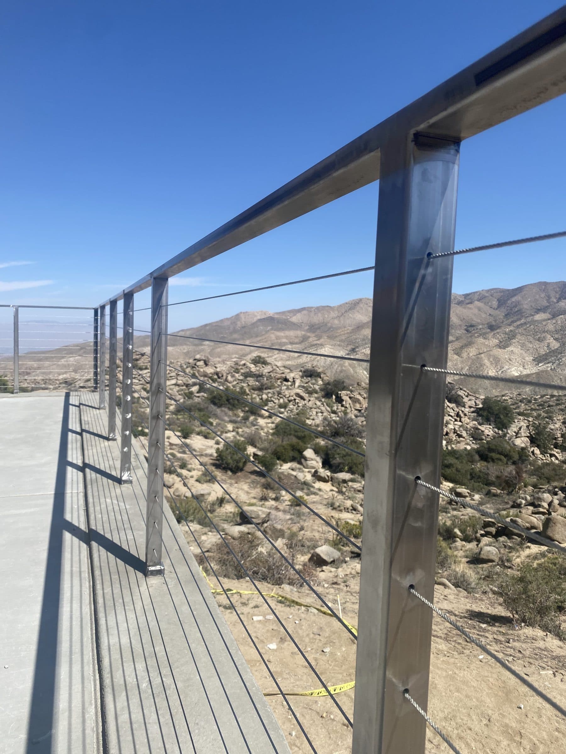 Stainless cable railing running along a deck edge toward boulder-covered slopes and mountains.