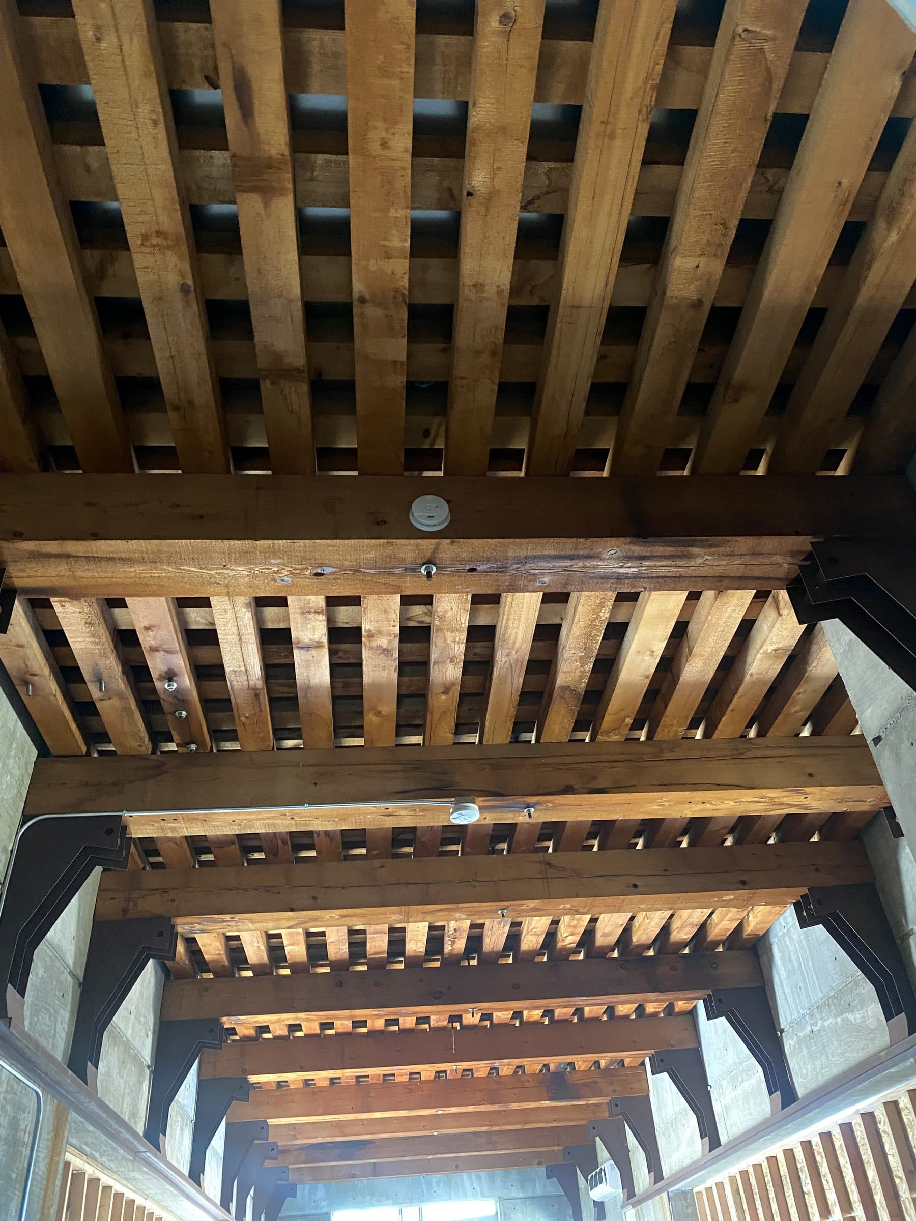 Heavy timber joist ceiling receding in layered rows down a concrete hall.