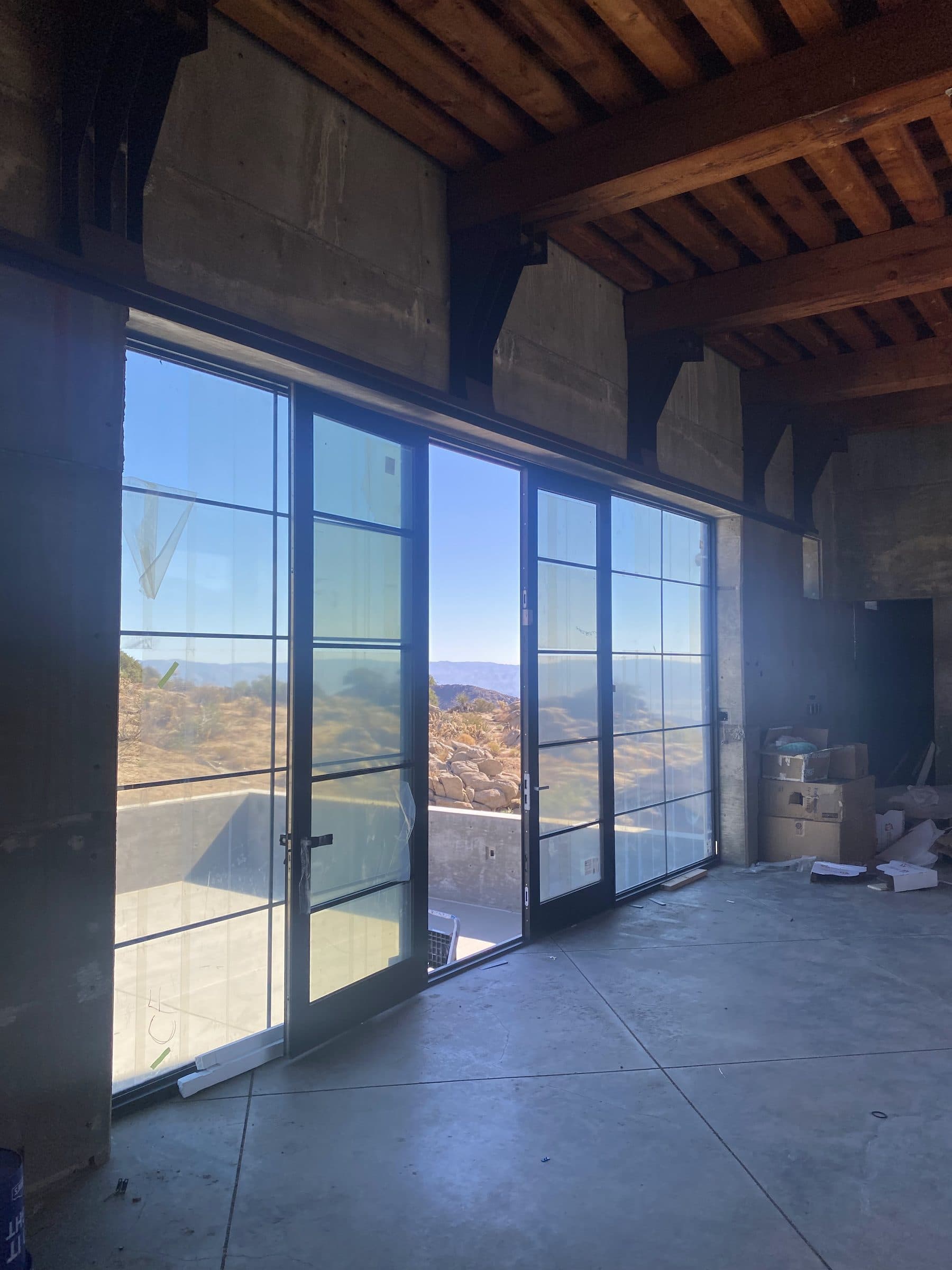 New black aluminum-framed glass wall and doors under timber joists, boxes staged against the far wall.