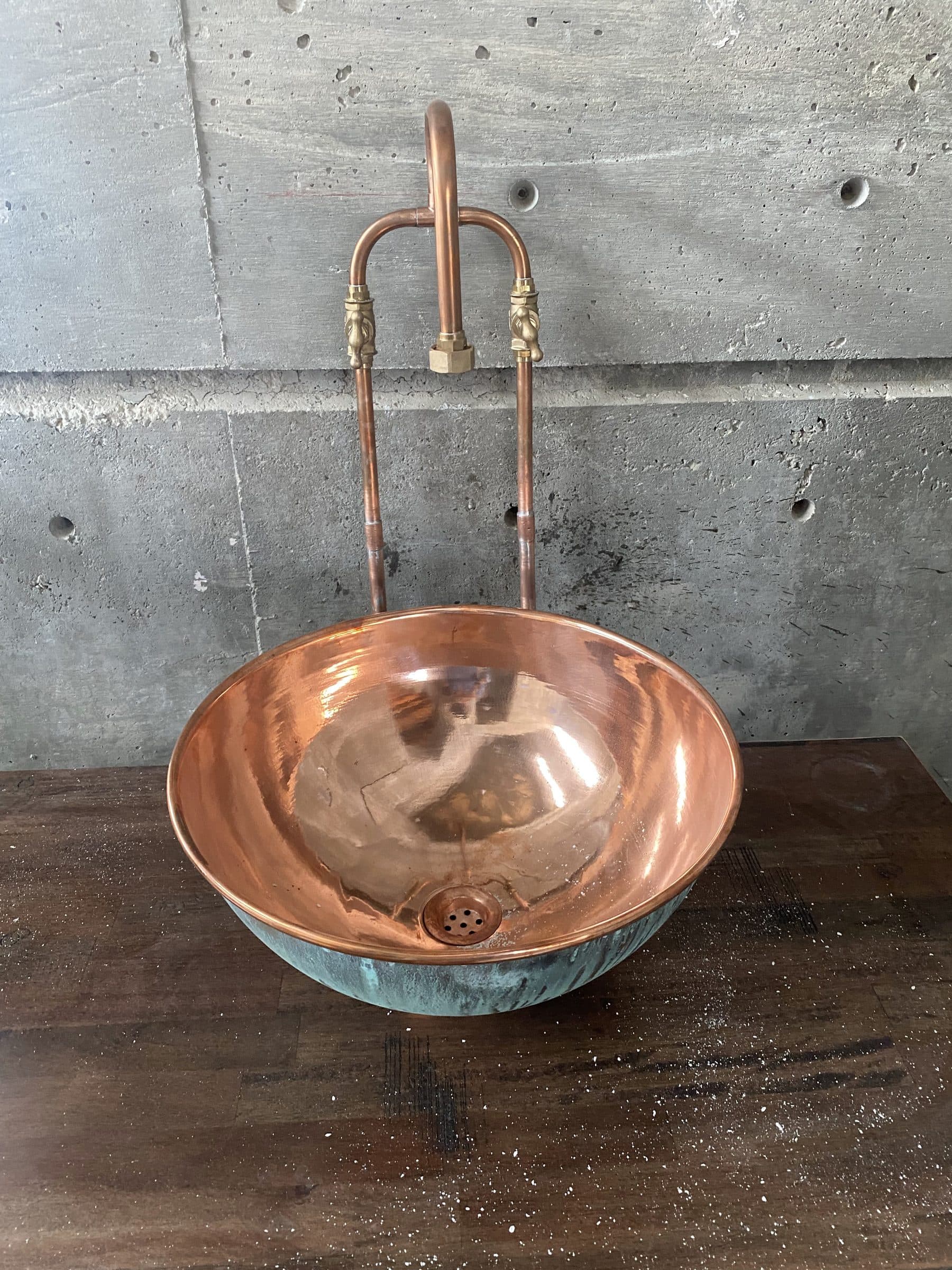 Verdigris copper basin with a looped bent-copper faucet against a board-formed concrete wall.