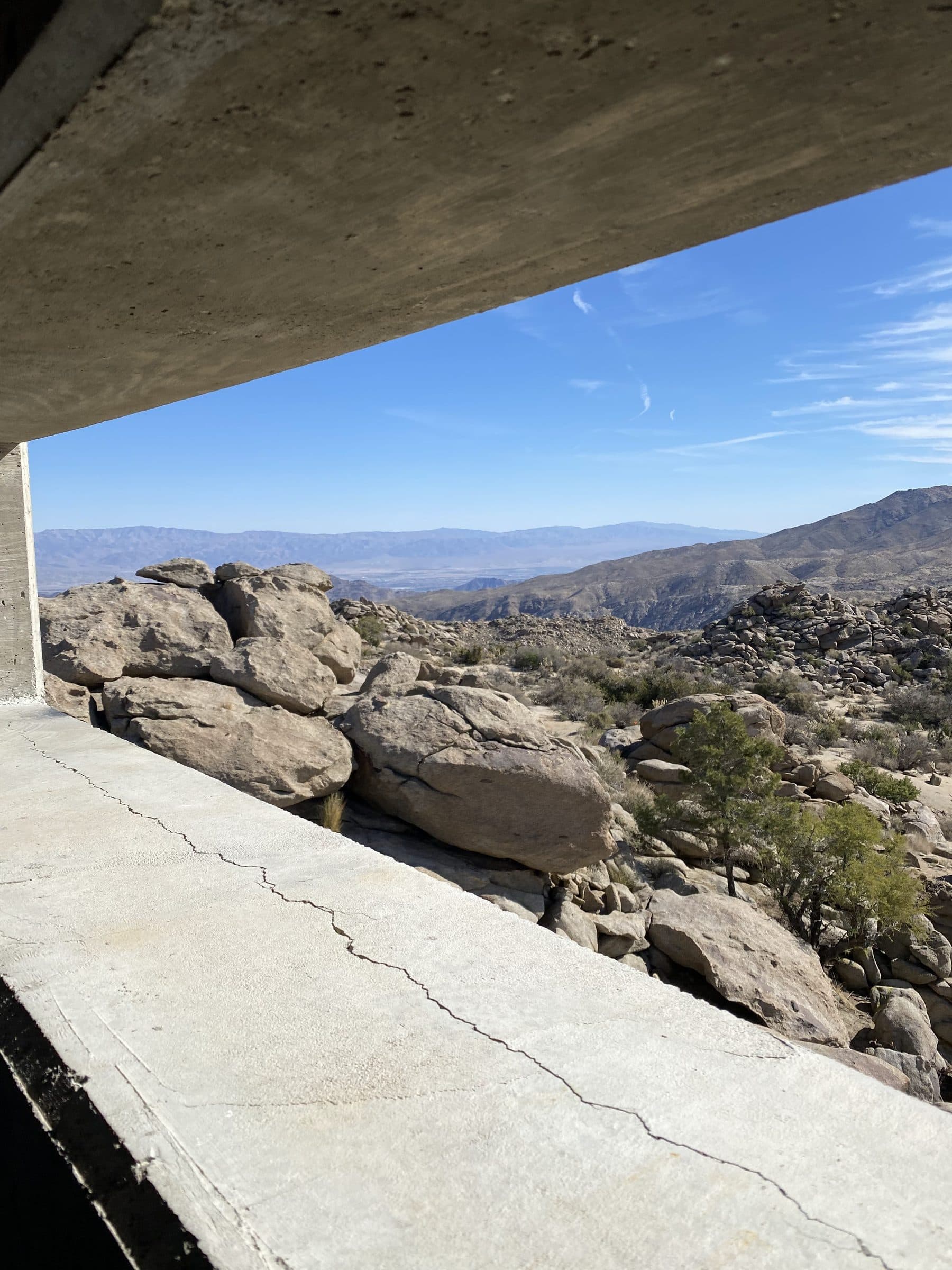Boulder field and hazy ranges framed between a concrete overhang and window ledge.