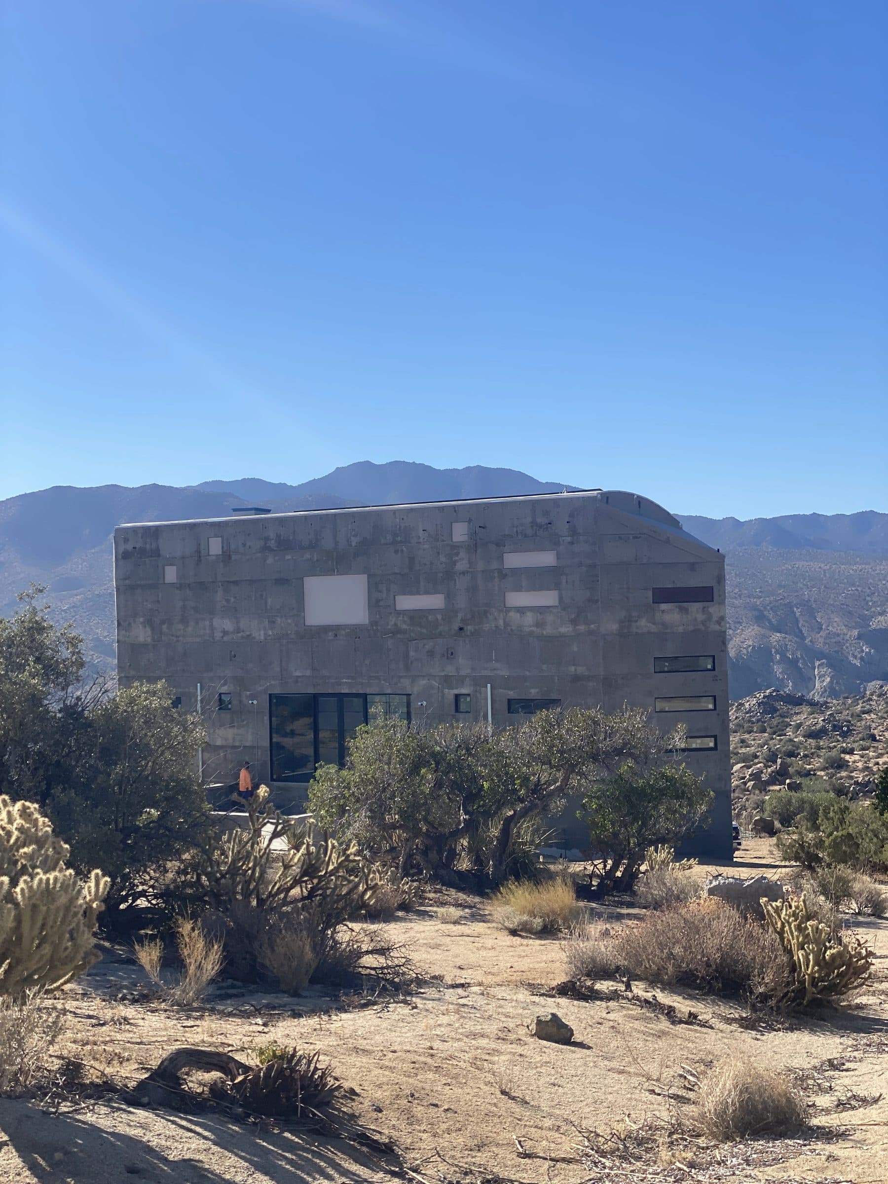 Concrete house among cholla and desert scrub, mountain ridges behind.