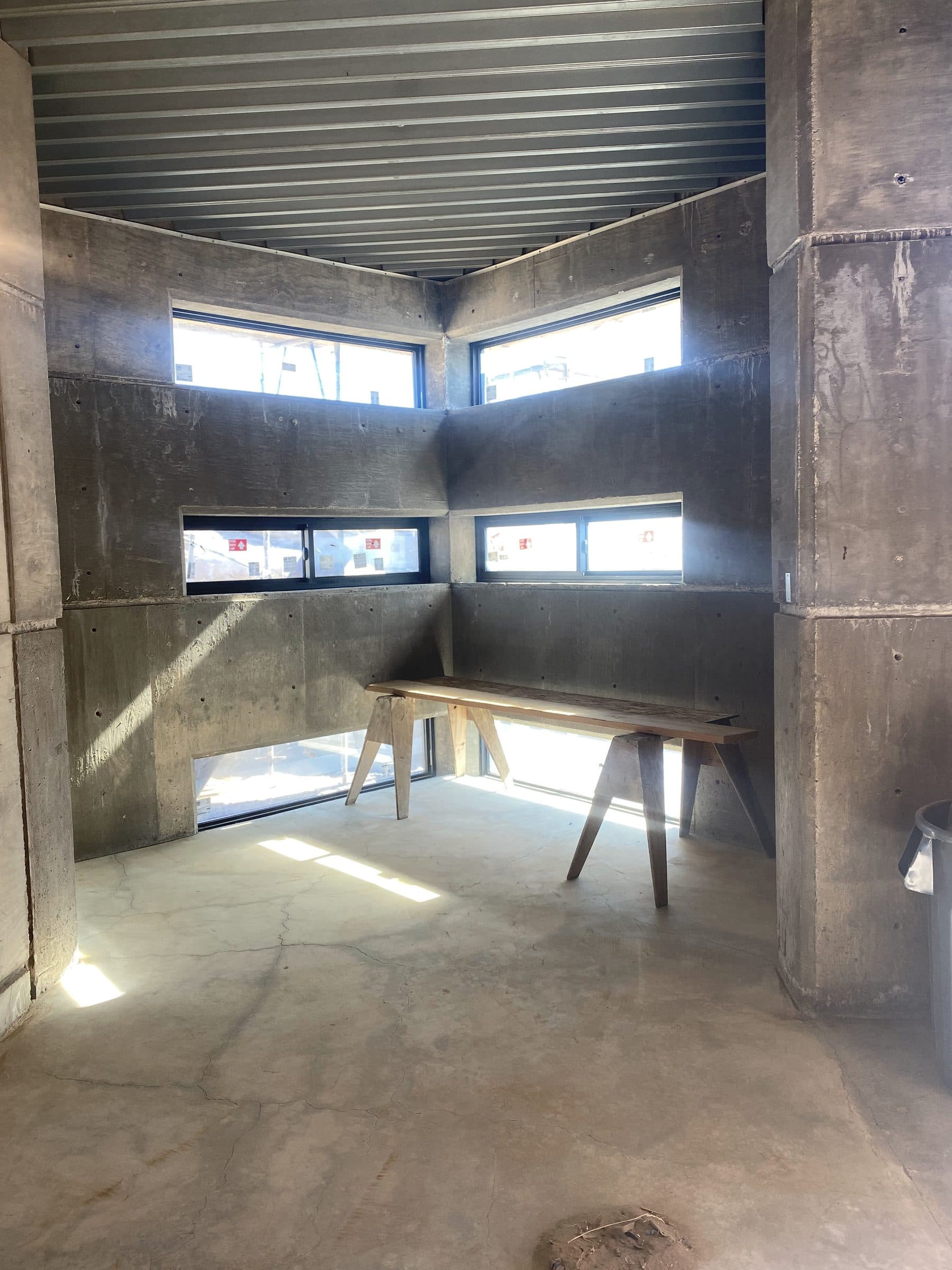 Corner room with a sawhorse bench under stacked window bands, raking light across the floor.