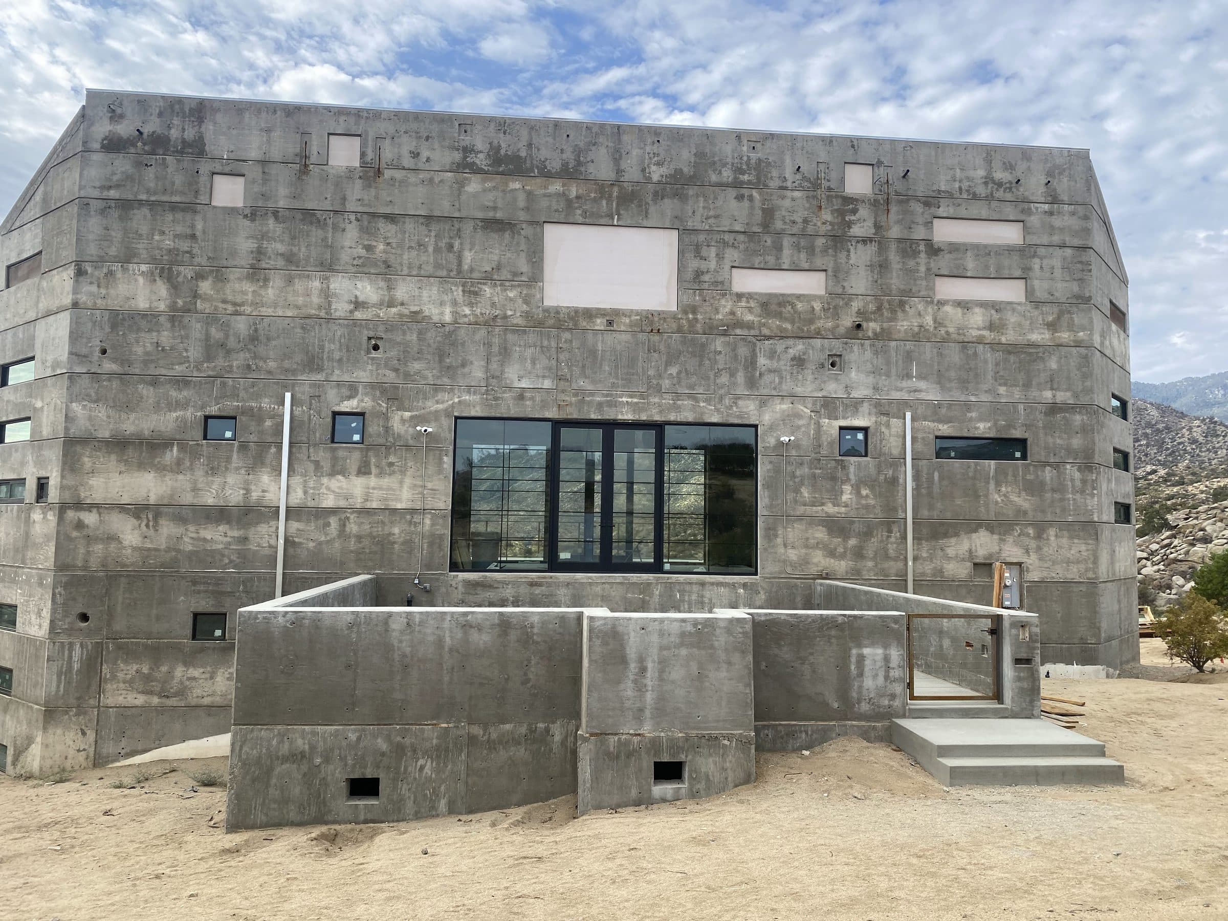 Rear elevation with cast courtyard walls and an aluminum-framed window and door wall at center.