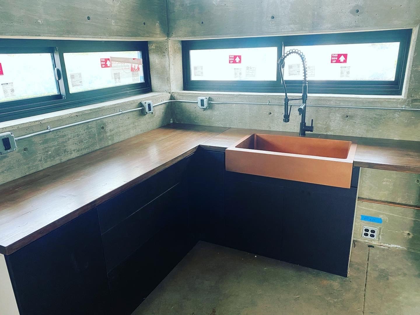 Kitchen corner with a copper farmhouse sink, dark cabinets, walnut counters, and ribbon windows on two sides.