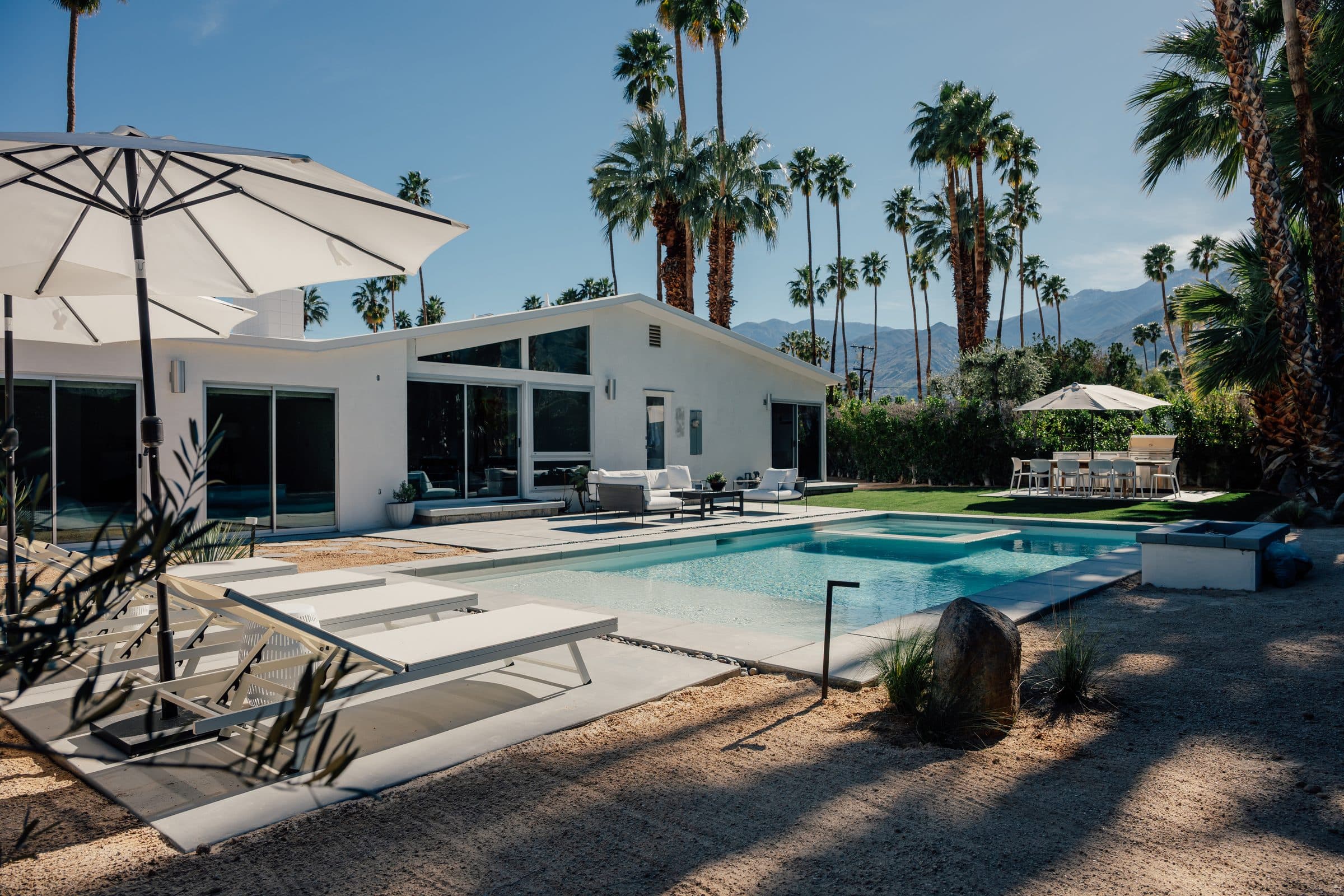 Full backyard panorama: the rear elevation, the pool, and the outdoor dining and lounge areas strung along the water.