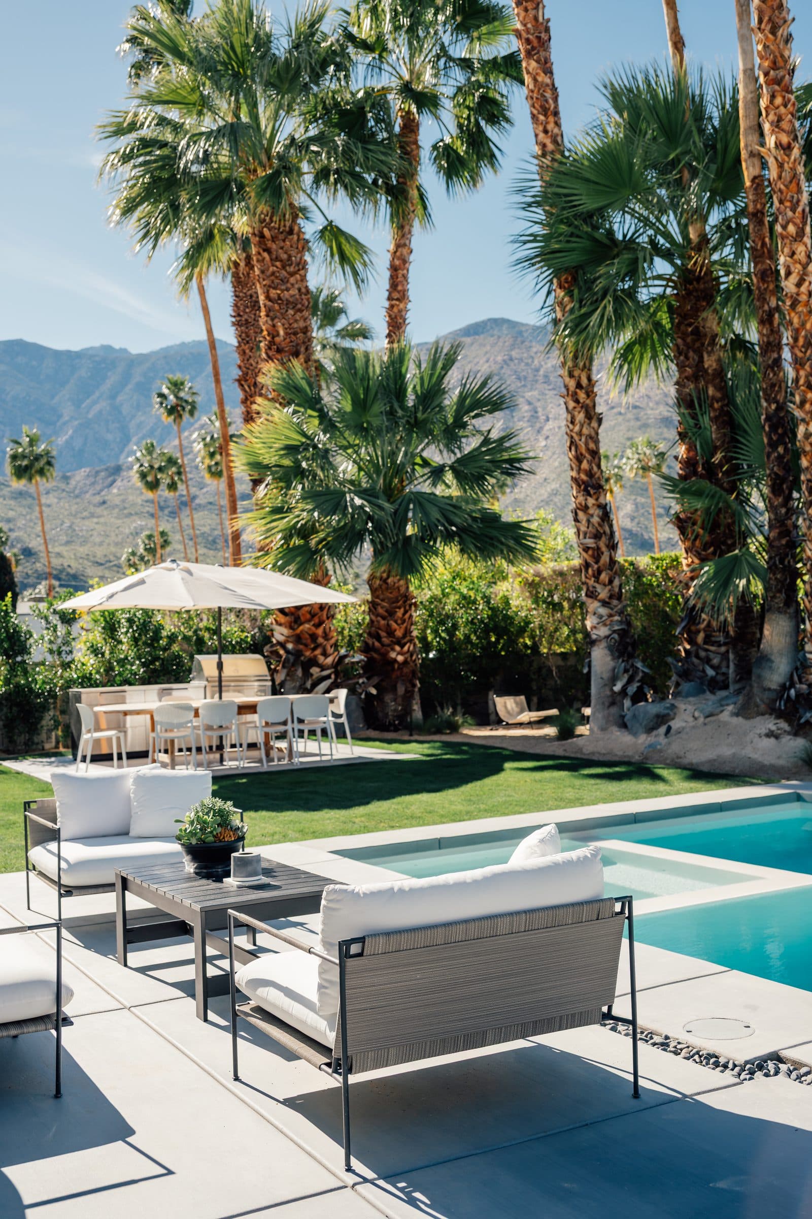 Lounge seating, the pool, and the outdoor dining patio in one view of the backyard, mountains beyond the palms.