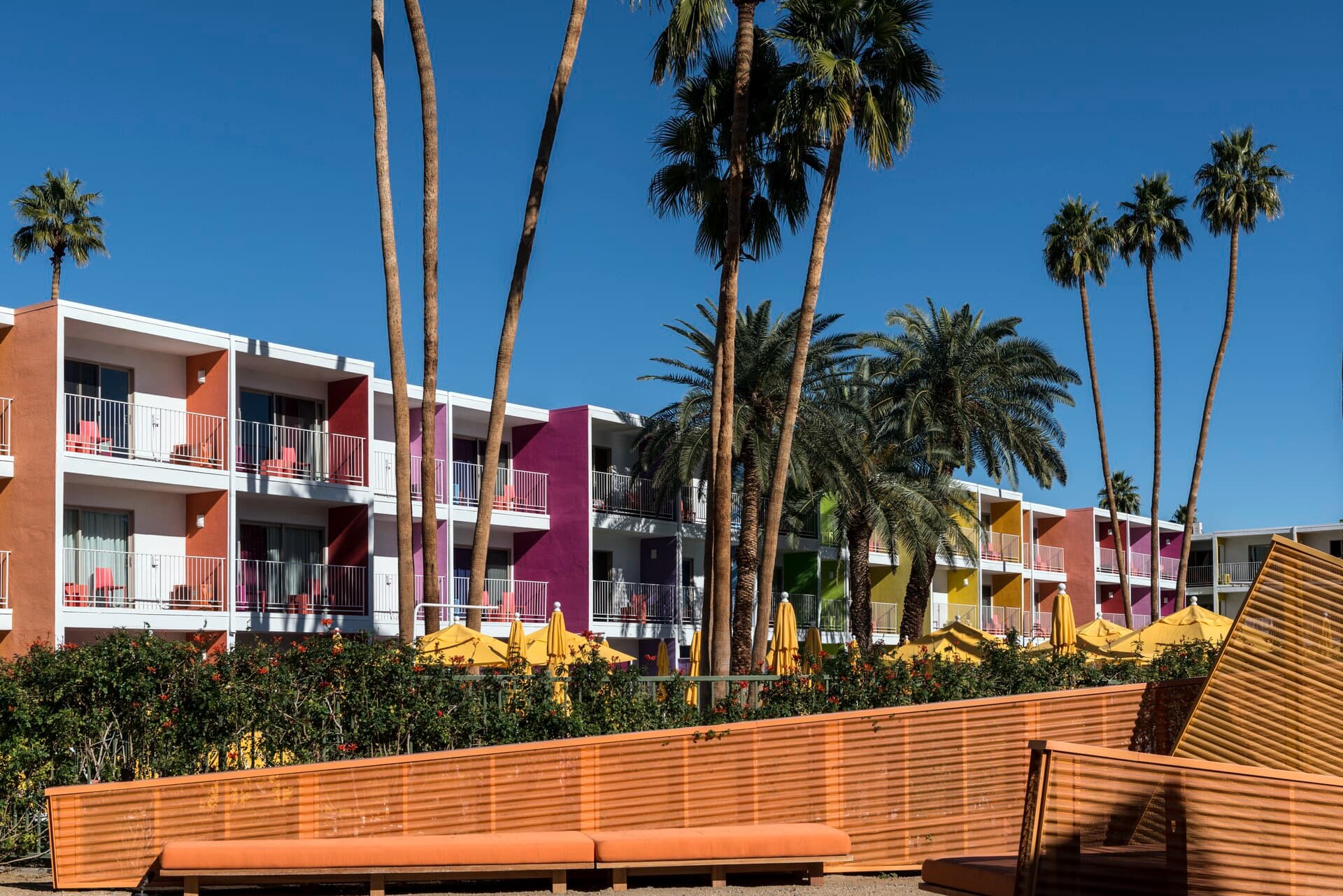 The Saguaro Palm Springs: multi-color striped façade with balconies, palms and yellow umbrellas
