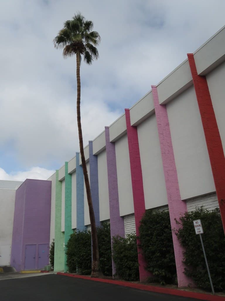 Green palm-frond cutout screens on a magenta and white façade, wildflowers below